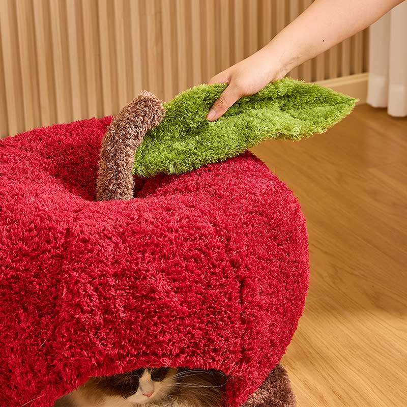 Apple Cat Cave Bed — Cozy, Cute, and Safe with a hand adjusting the green leaf on a soft red apple-shaped bed.