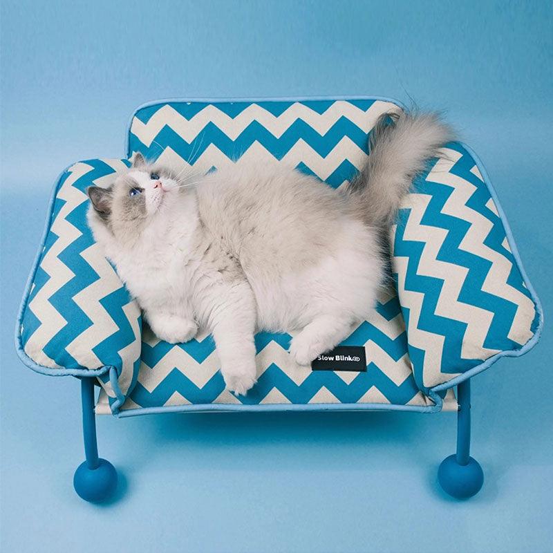 A fluffy cat lounging comfortably on a Memphis-Style Elevated Cat Hammock with a zigzag blue design.